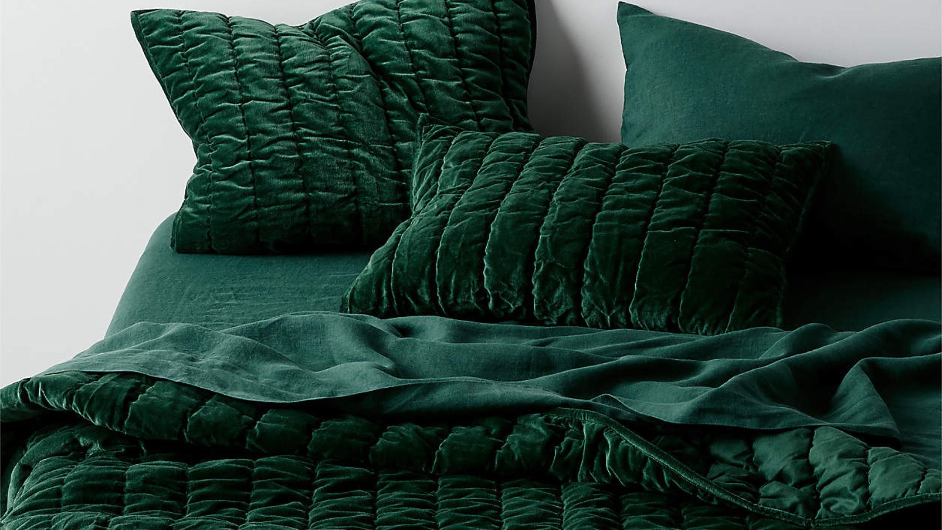 A bed made up with Crate & Barrel's velvet cotton green quilt and green sheets and pillowcases for Christmas bedding.
