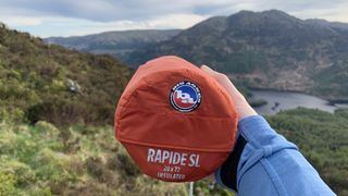 Hand holding the Big Agnes Rapide SL sleeping pad in its stuff sack with mountains in background