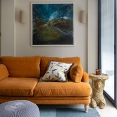 A living room with an orange velvet sofa, an abstract painting hanging above and a bear-shaped side table