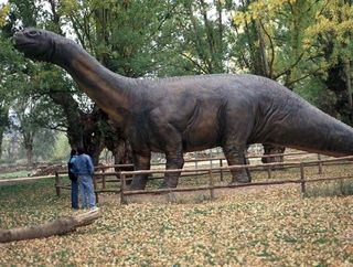 Visitors look at a model of a sauropod dinosaur.