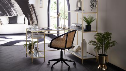 A modern black, white and gold home office with paintstroke wall decor, gold ladder desk and gold shelving unit