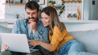 Happy couple sitting on sofa, looking at laptop