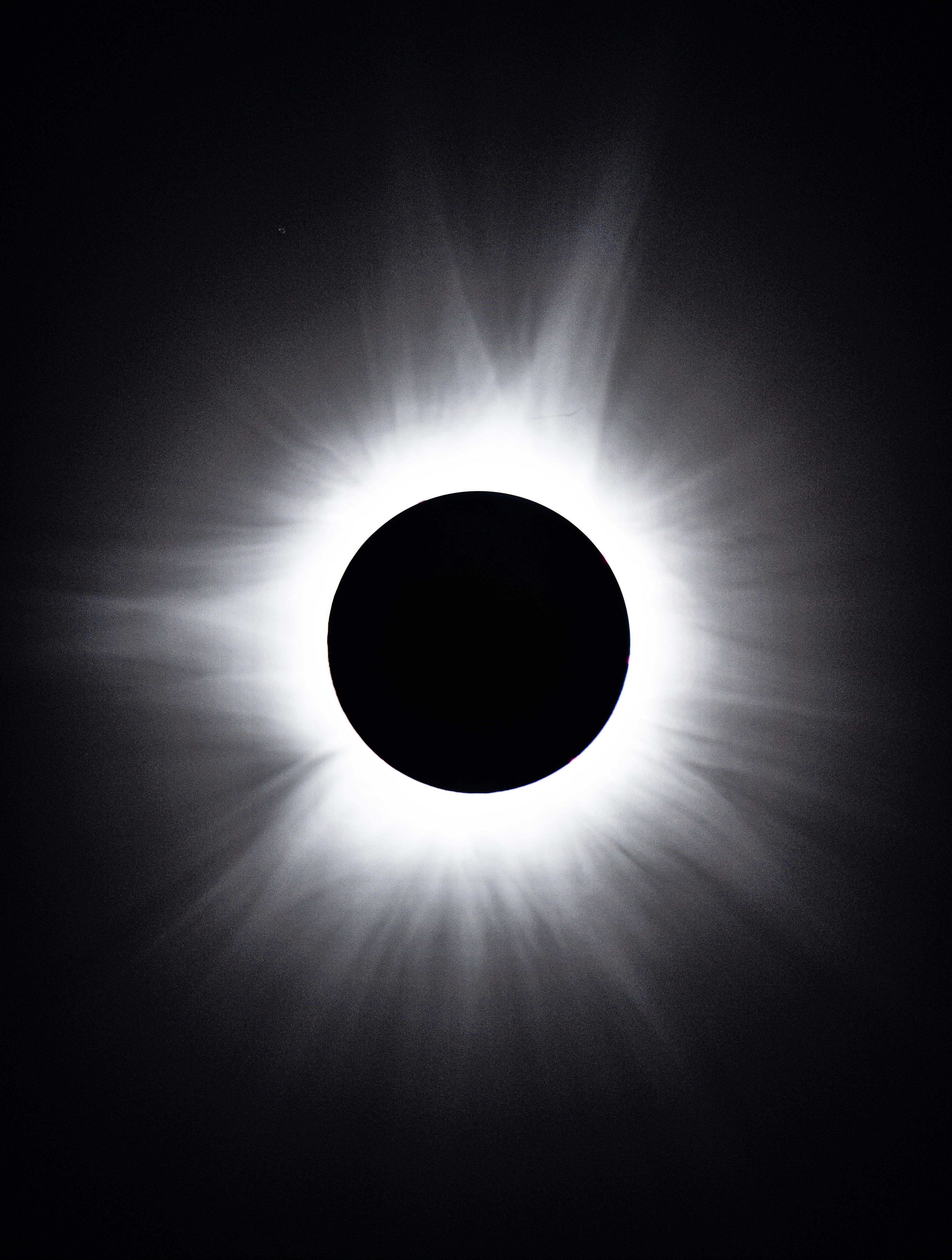 a black circle in the center which is the sun covered by the moon with a large white halo surrounding it, this is the corona, the sun's outer atmosphere.