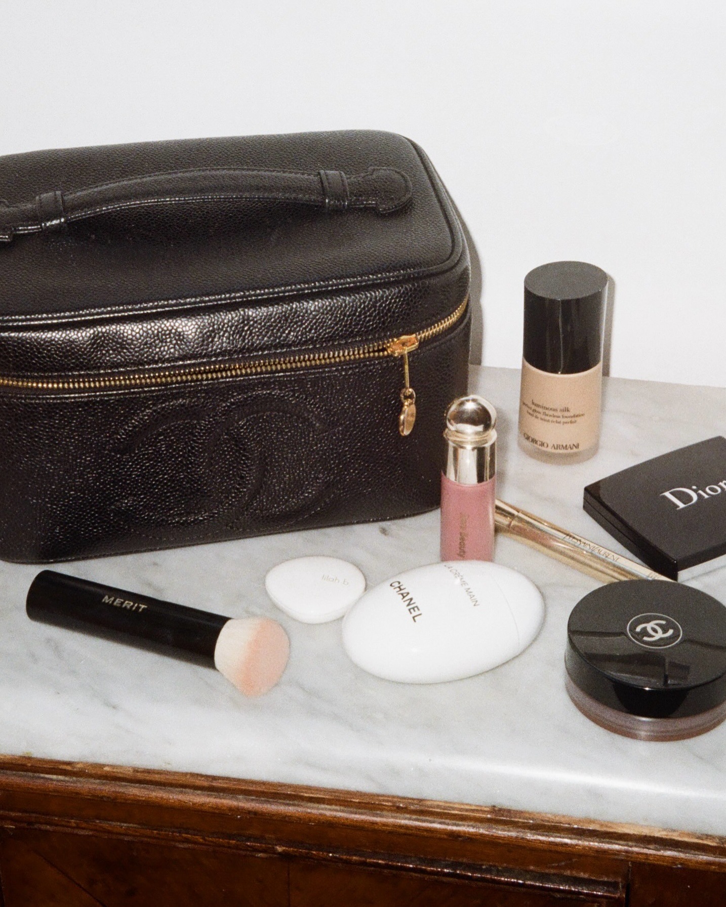 Chanel toiletry bag with makeup and skincare products on marble table
