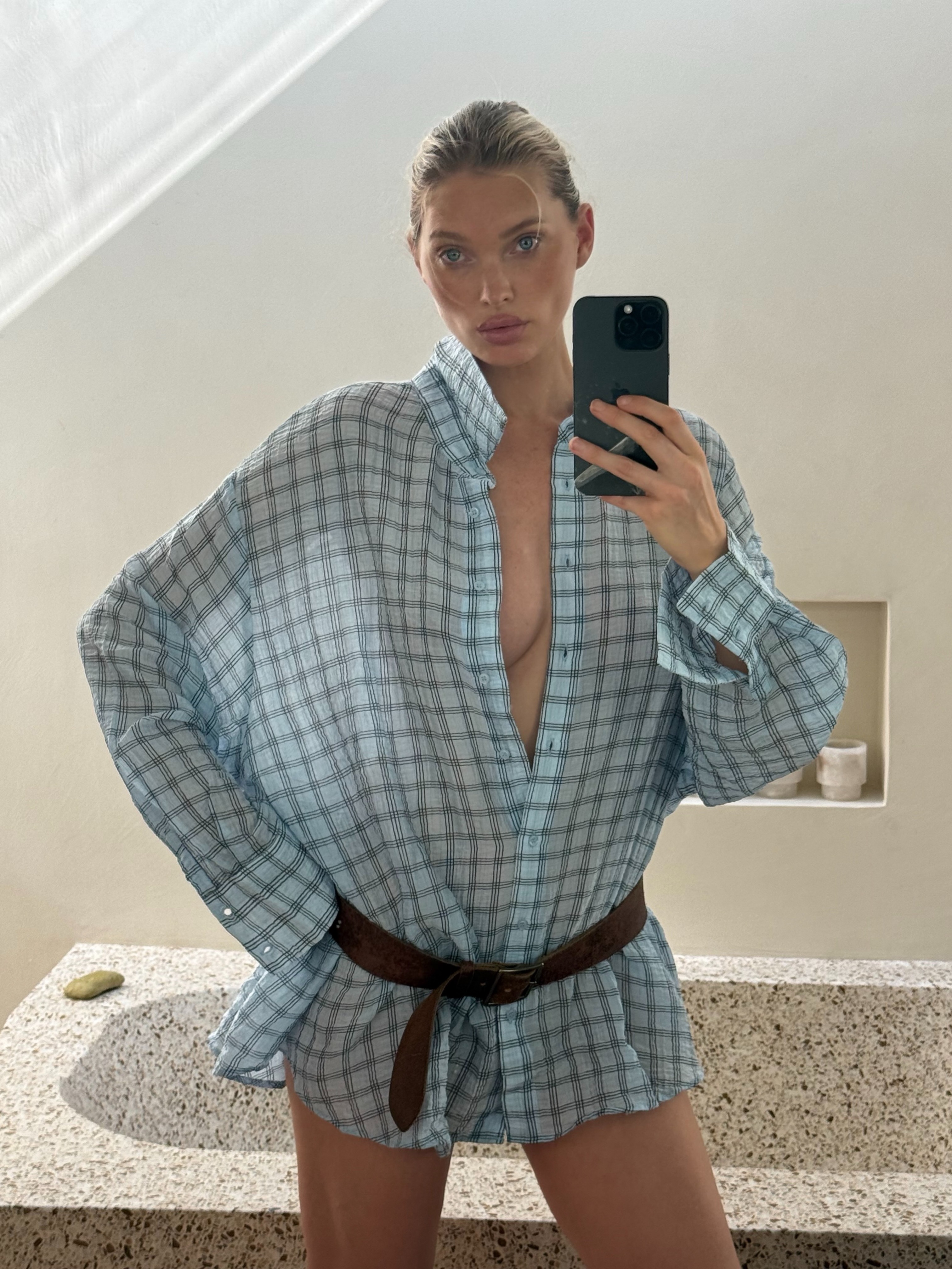 Model Elsa Hosk takes a mirror selfie wearing Mango's sheer blue checked shirt with a leather belt.