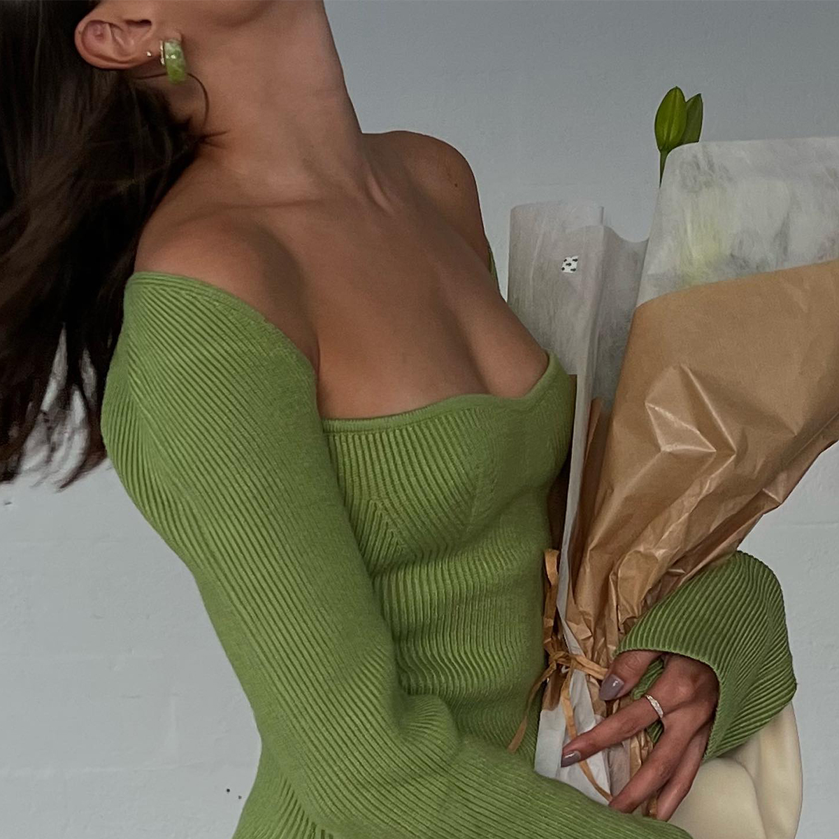 Woman wearing a green off the shoulder top holding a bouquet of flowers
