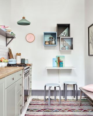 White kitchen with wall-mounted space-saving table and low stools on the end wall painted in Dulux's White cotton paint color