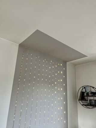 A white wall with a grey painted ceiling and fairy lights.
