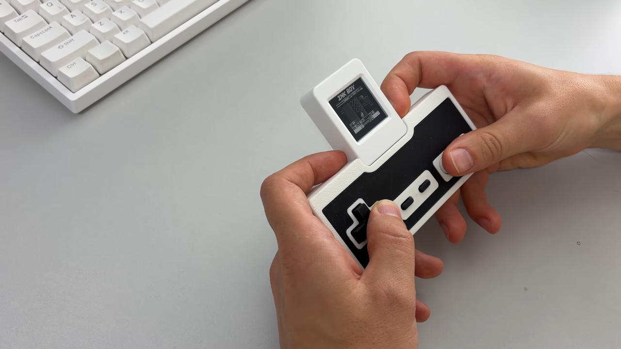 Hands using Ink-Boy docked on NES controller to play games at a desk.