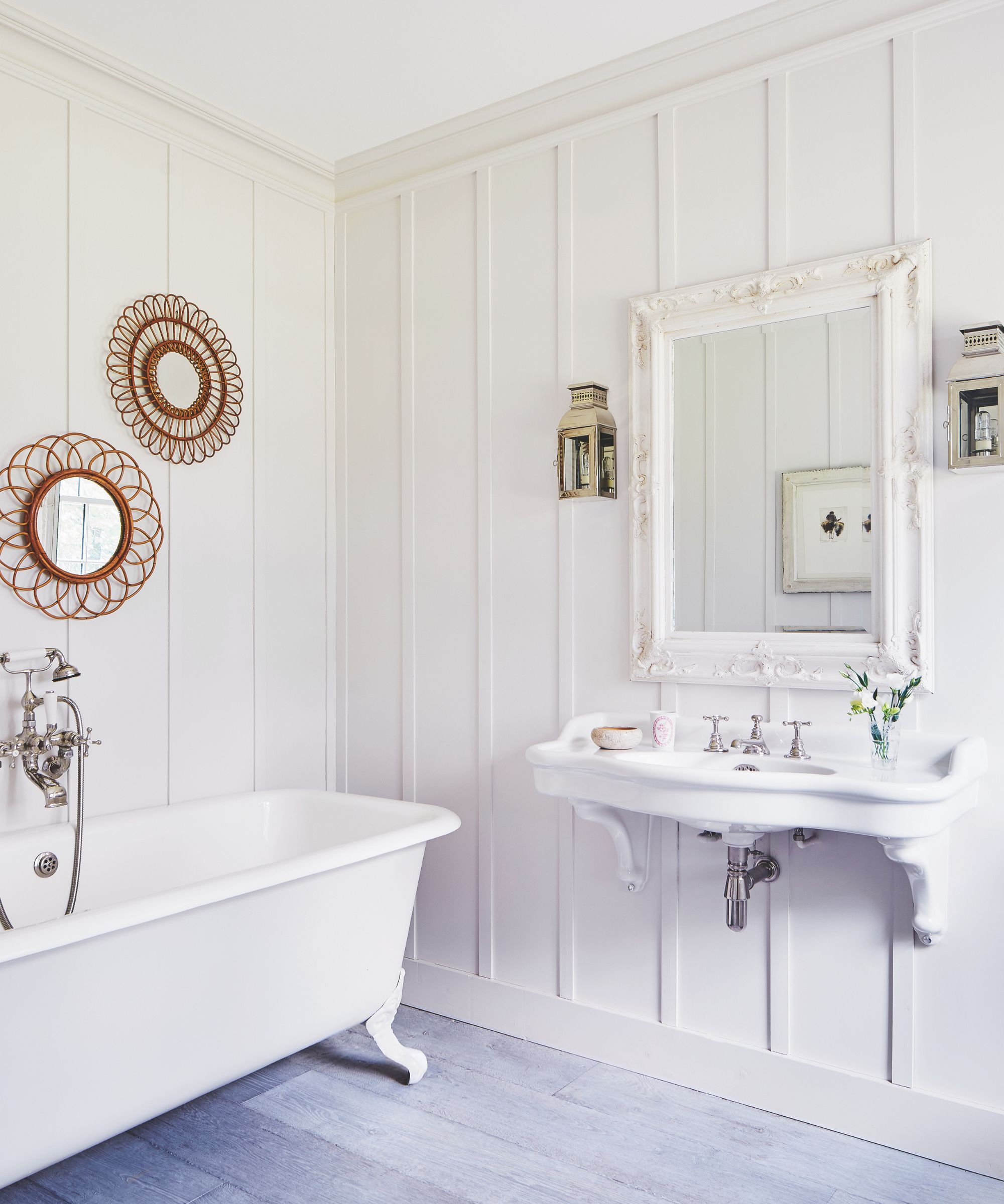 A white panelled bathroom with white bathtub, white mirror, white sink and wooden circular decorative mirrors on the wall.