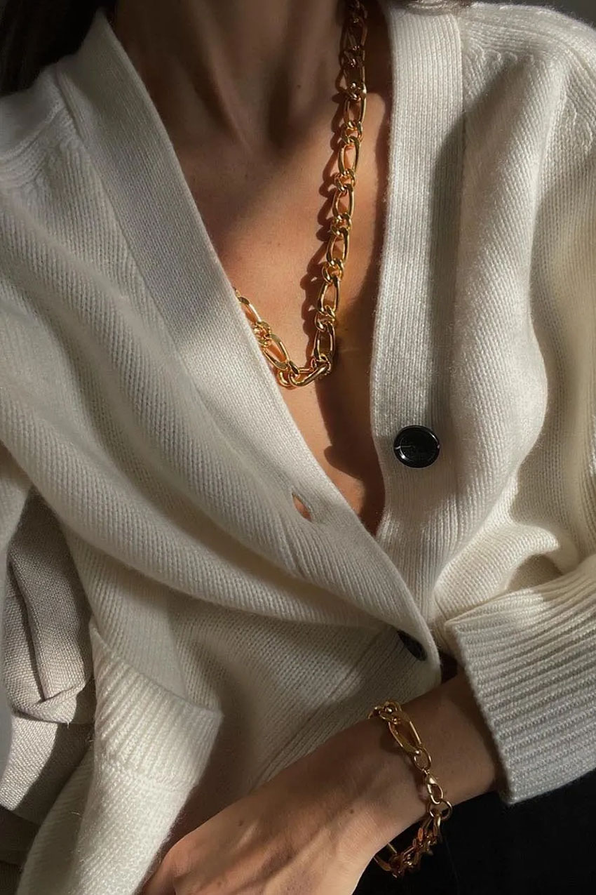 a woman wearing a sweater, chainlink necklace, and chainlink bracelet