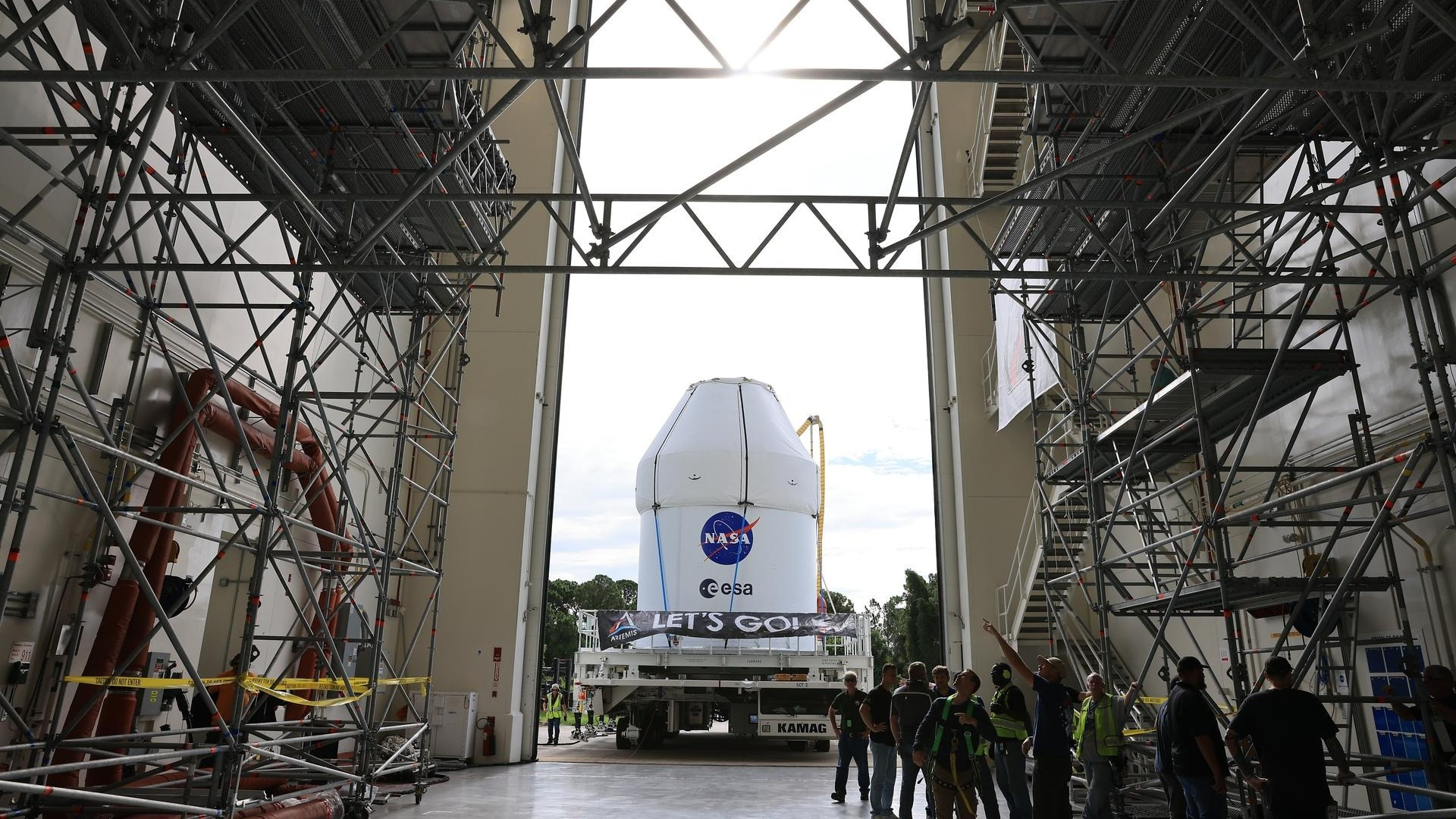 A white conical craft is carted through an open factory door.