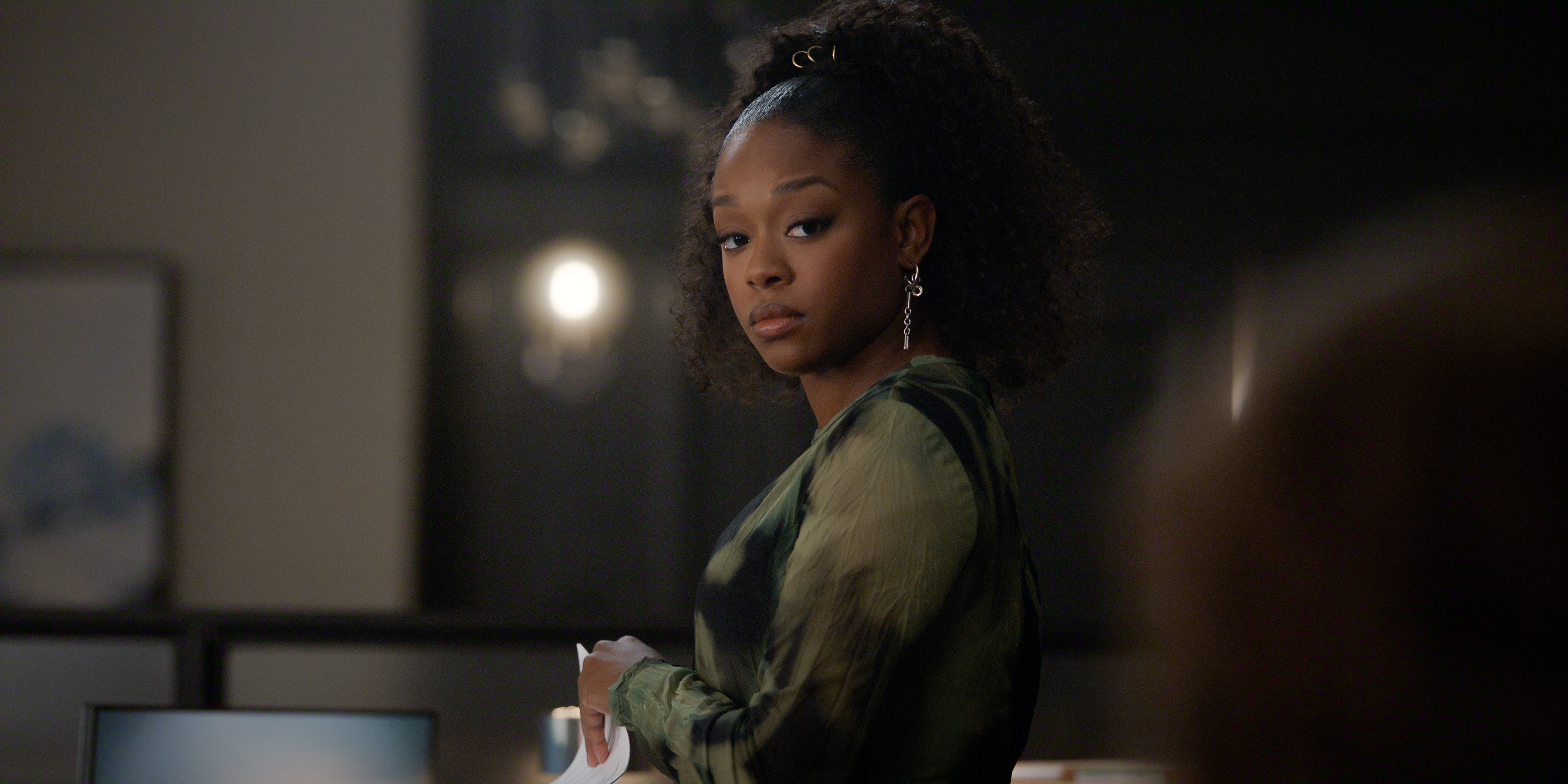 Jazz Raycole as Izzy Letts in episode 407 of The Lincoln Lawyer wearing a green printed shirt looking over her shoulder in an office
