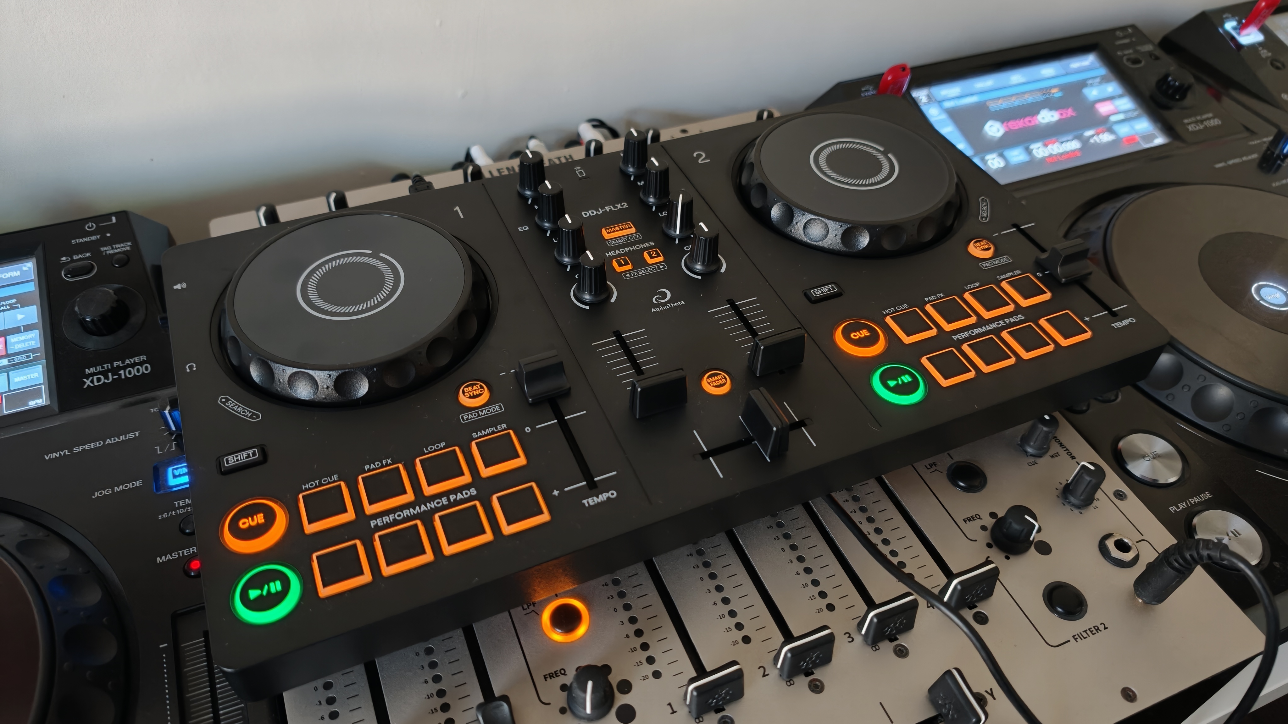 The DDJ-FLX2 resting on a larger DJ mixer, with media players on either side