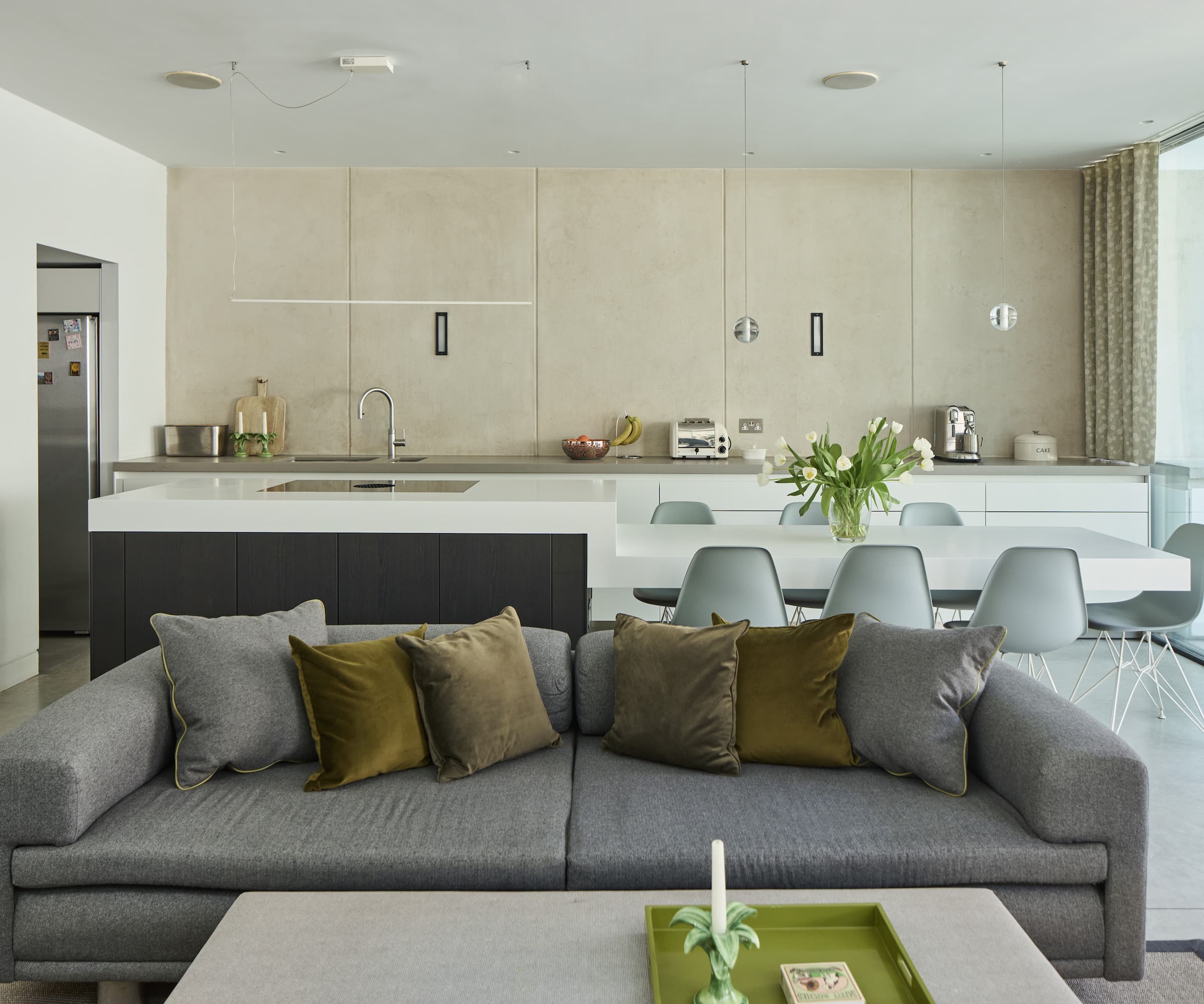 A kitchen-dining area with a grey sofa and kitchen island with white dining table and marble walls