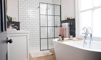 white bathroom with black framed shower screen, chrome shower head and Victorian radiator with freestanding bath tub and traditional mixer tap