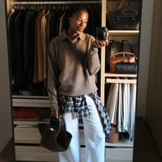 taffy msipa wears a brown jacket, check shirt and white jeans in front of her wardrobe