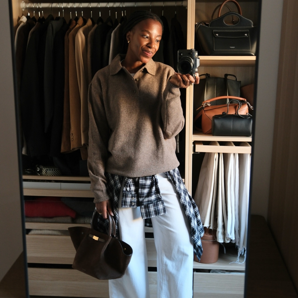 taffy msipa wears a brown jacket, check shirt and white jeans in front of her wardrobe