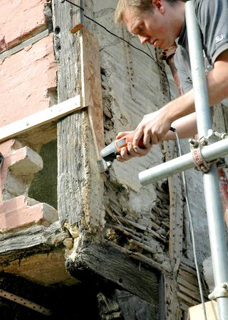 Making repairs to a timber frame building. Traditional wattle and daub can be seen between the timbers