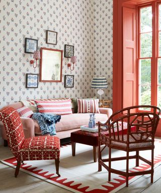 red and white living room with patterned wallpaper and painted window frame and a pink sofa with two occasional chairs