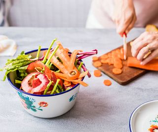 Person cuts carrots and collects vegetable scraps in bowl on counter