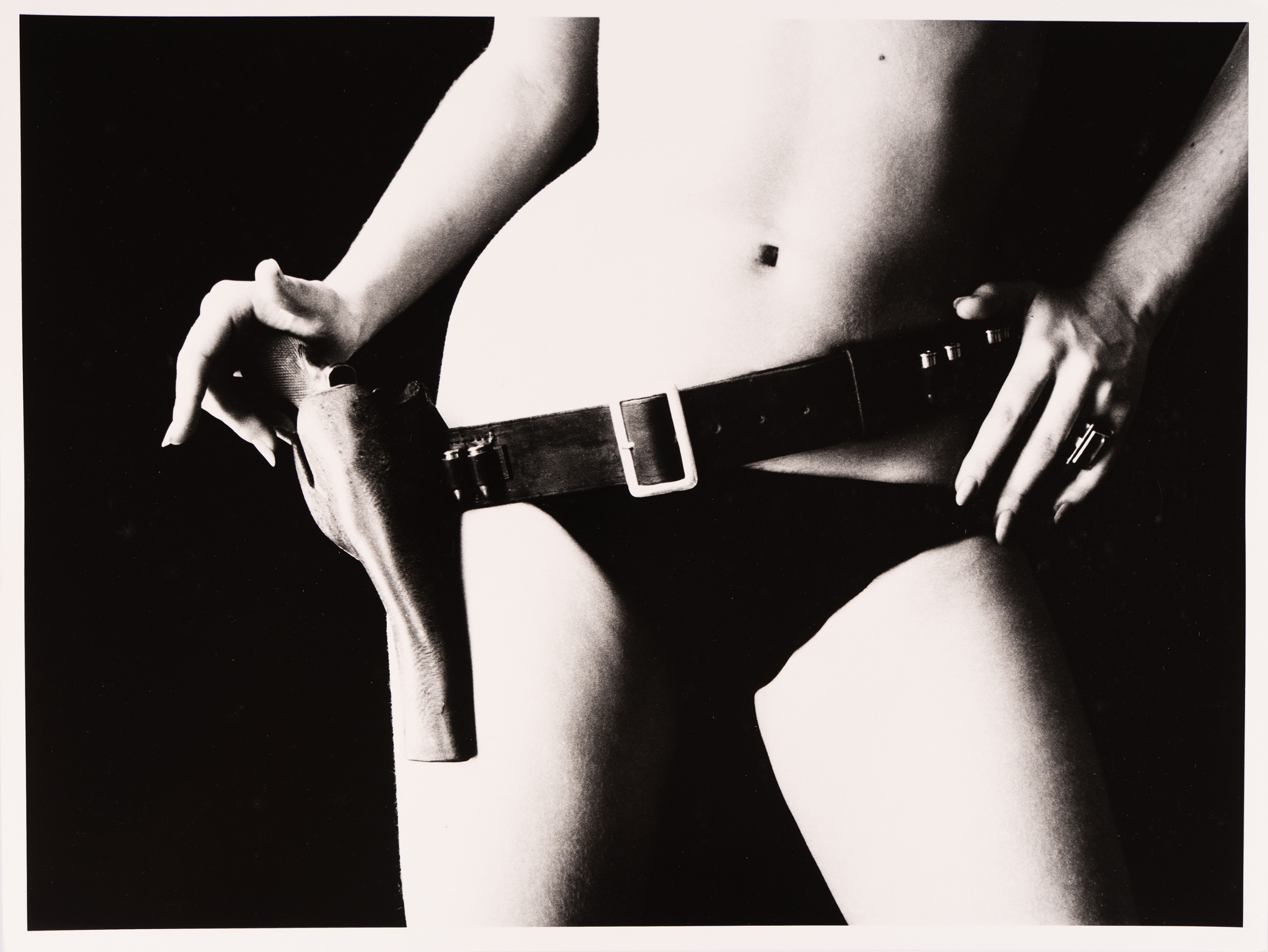 A close cropped shot of bare hips and thighs wearing a gun belt and holster, with two hands resting on the buckle and holster.