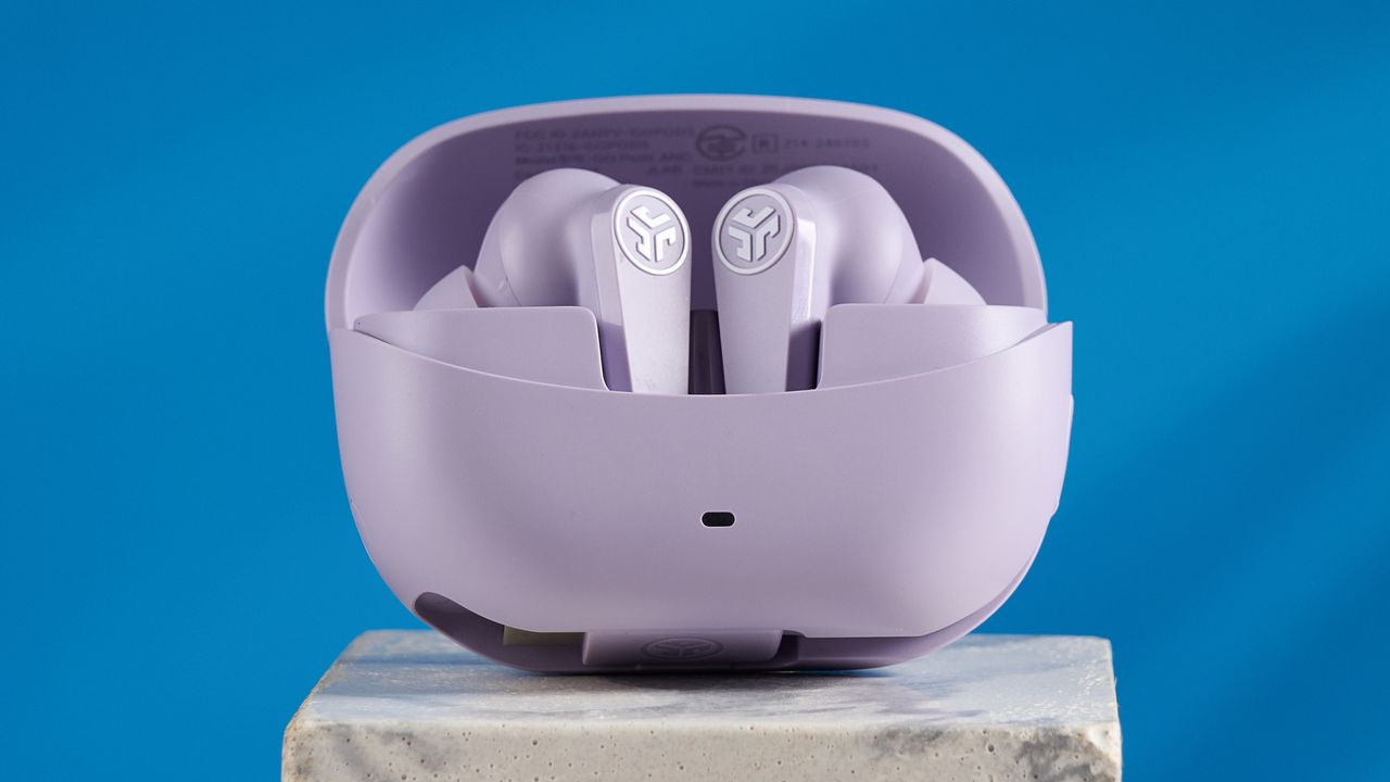 the jlab go pods anc earbuds in lilac with a lilac charging case and built in usb-c cable against a blue background on a marble stand
