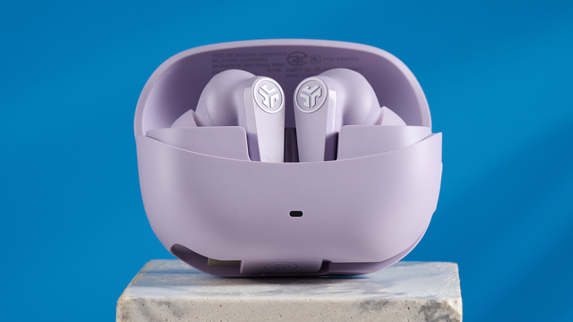 the jlab go pods anc earbuds in lilac with a lilac charging case and built in usb-c cable against a blue background on a marble stand