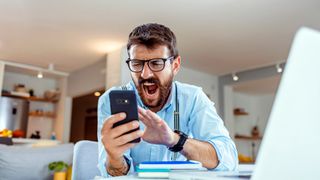 Angry man shouting at mobile phone while sitting at a desk