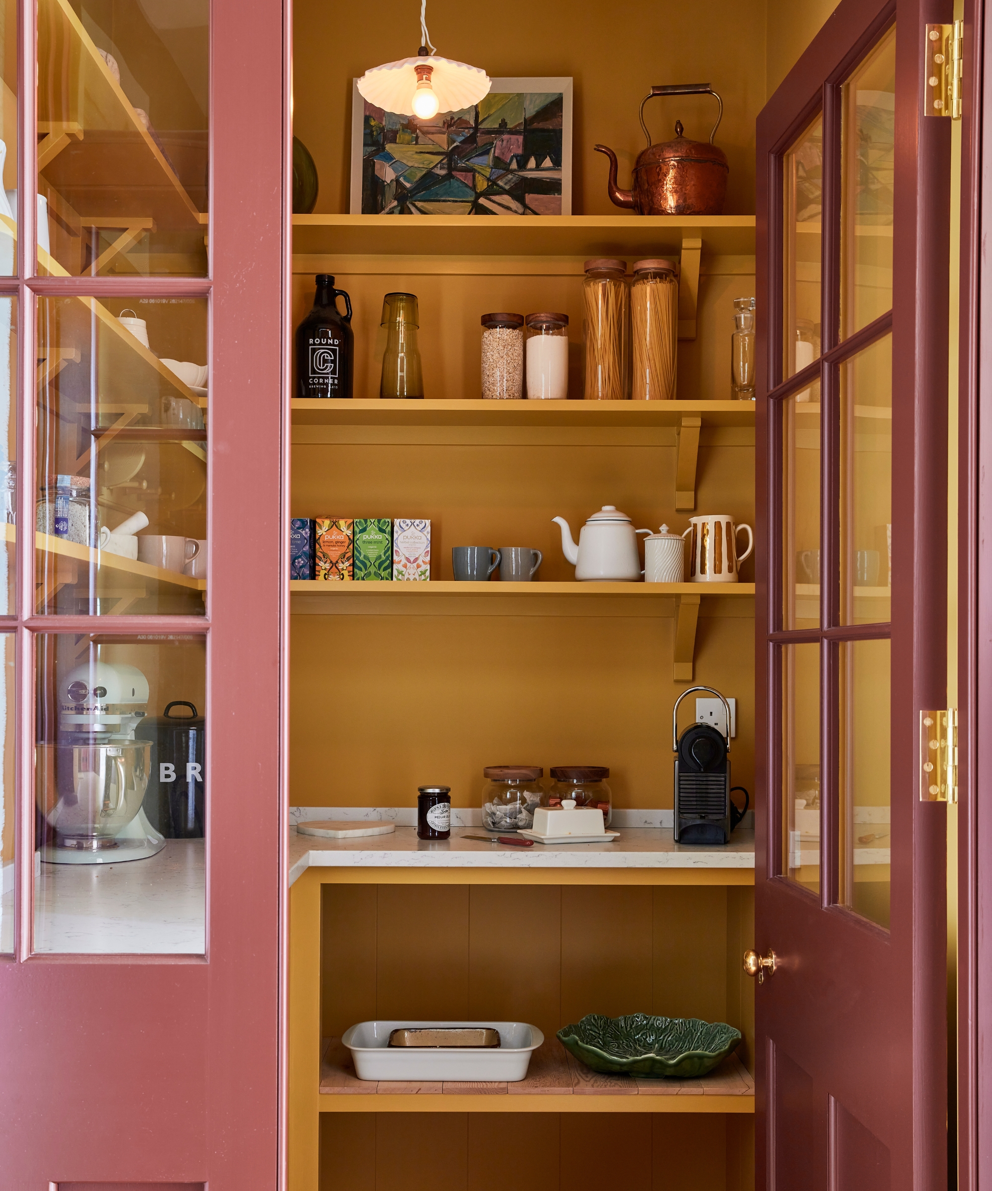 A small pantry with muddy red doors and a bold yellow interior