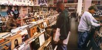 The gatefold cover of Endtroducing by DJ Shadow. It shows three people browsing the racks in a large record shop. A tortoiseshell cat is sitting on top of one of the racks on the left.
