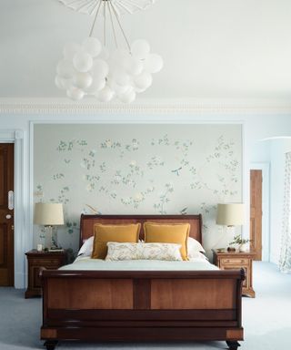 pastel blue bedroom with wooden bed, floral wall mural, white globe pendant and yellow velvet cushions