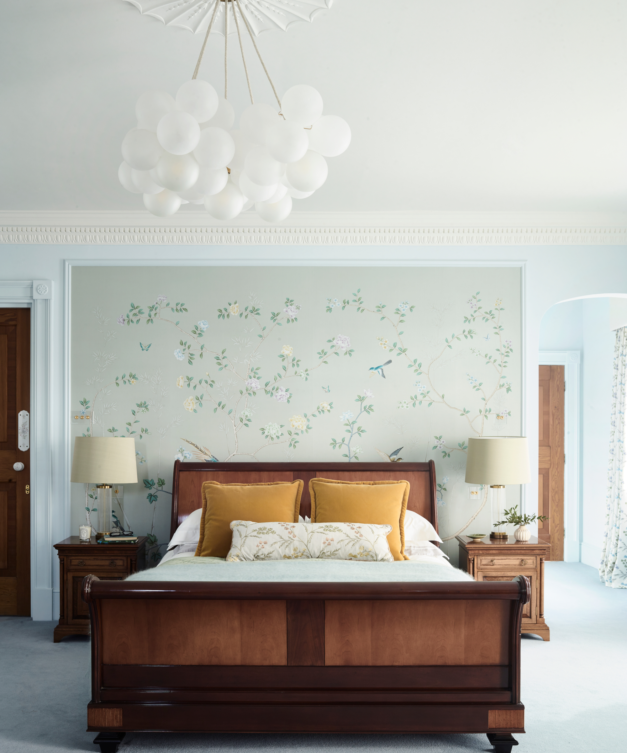 chambre bleu pastel avec lit en bois, décoration murale florale, pendentif globe blanc et coussins en velours jaune