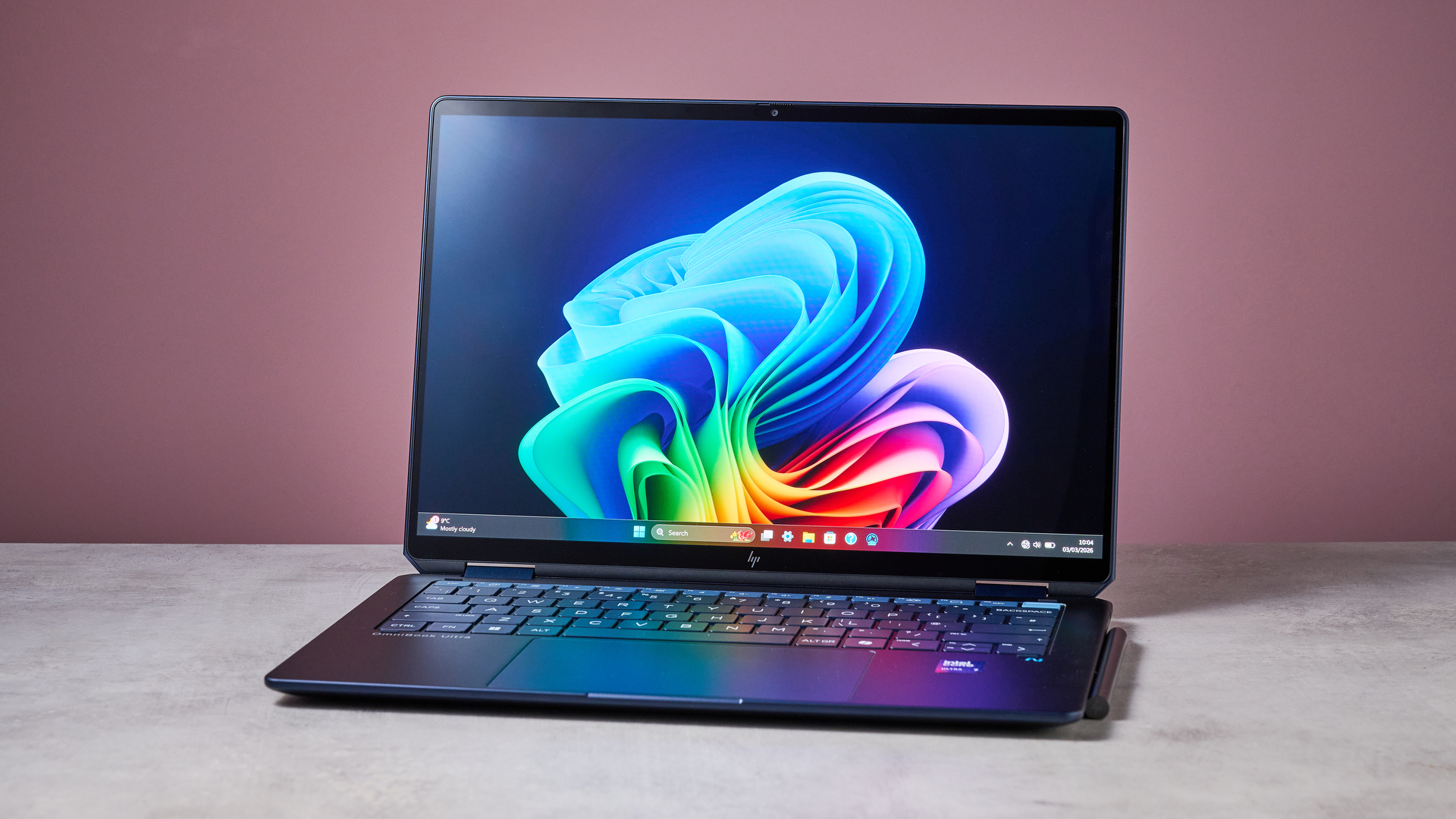 Three-quarter view of HP OmniBook Ultra Flip 14 open on white desk with pink wall in background