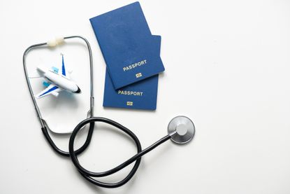 A stethoscope, toy plane and passport on a grey background.
