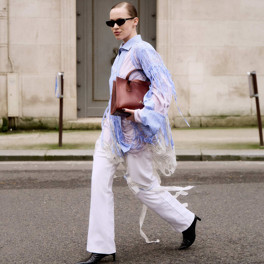 Woman wears distressed blue button down white jeans and black boots while carrying a brown ntote bag