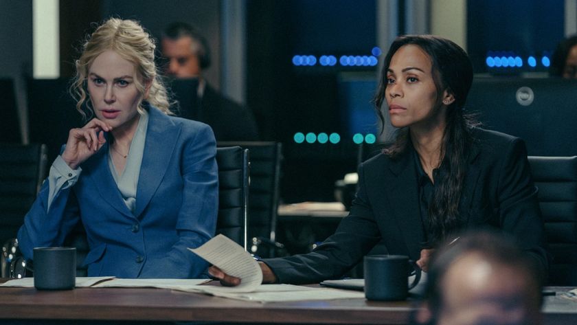 From left to right: Nicole Kidman sitting with her left elbow on her table and her hand on her chin and Zoe Saldana looking forward while lifting a paper with her left hand. 