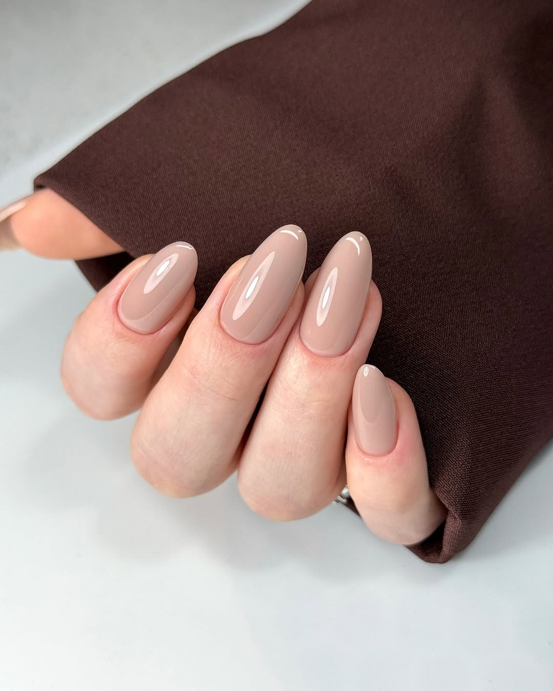 Close-up photo of a person&amp;rsquo;s hand showcasing glossy nude painted almond-shaped nails.