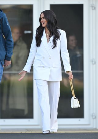 Meghan Markle wears a white suit and carries a Valentino bag