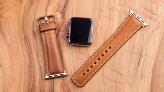 An Apple Watch with the leather band removed on a wooden background