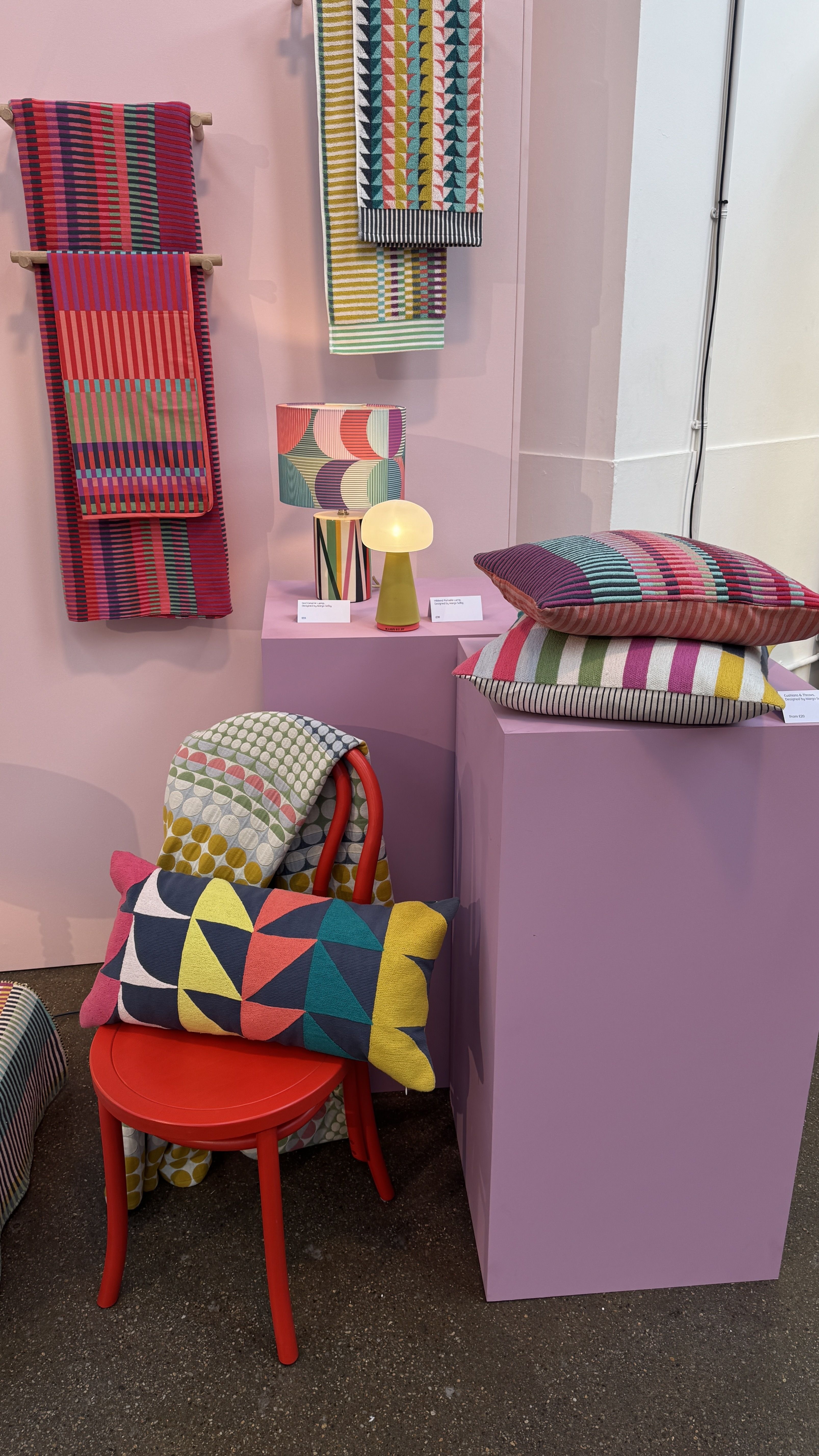 colorful cushions and towels on a pink wall and pink plinth and red chair