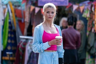 EastEnders Lola Pearce holding a coffee wearing a bright pink crop top with a velvet tracksuit