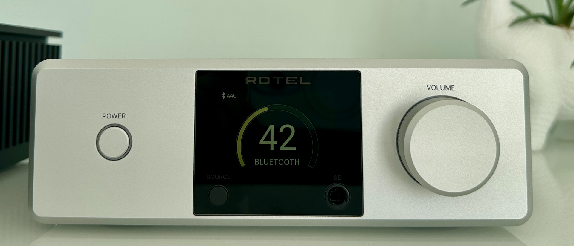 Rotel's DX-5 integrated amp in silver on a light gray table, with the amp's remote visible