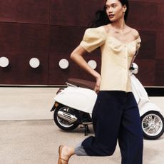 Woman crossing the street wearing neutral tailored outfit with white motorbike in background