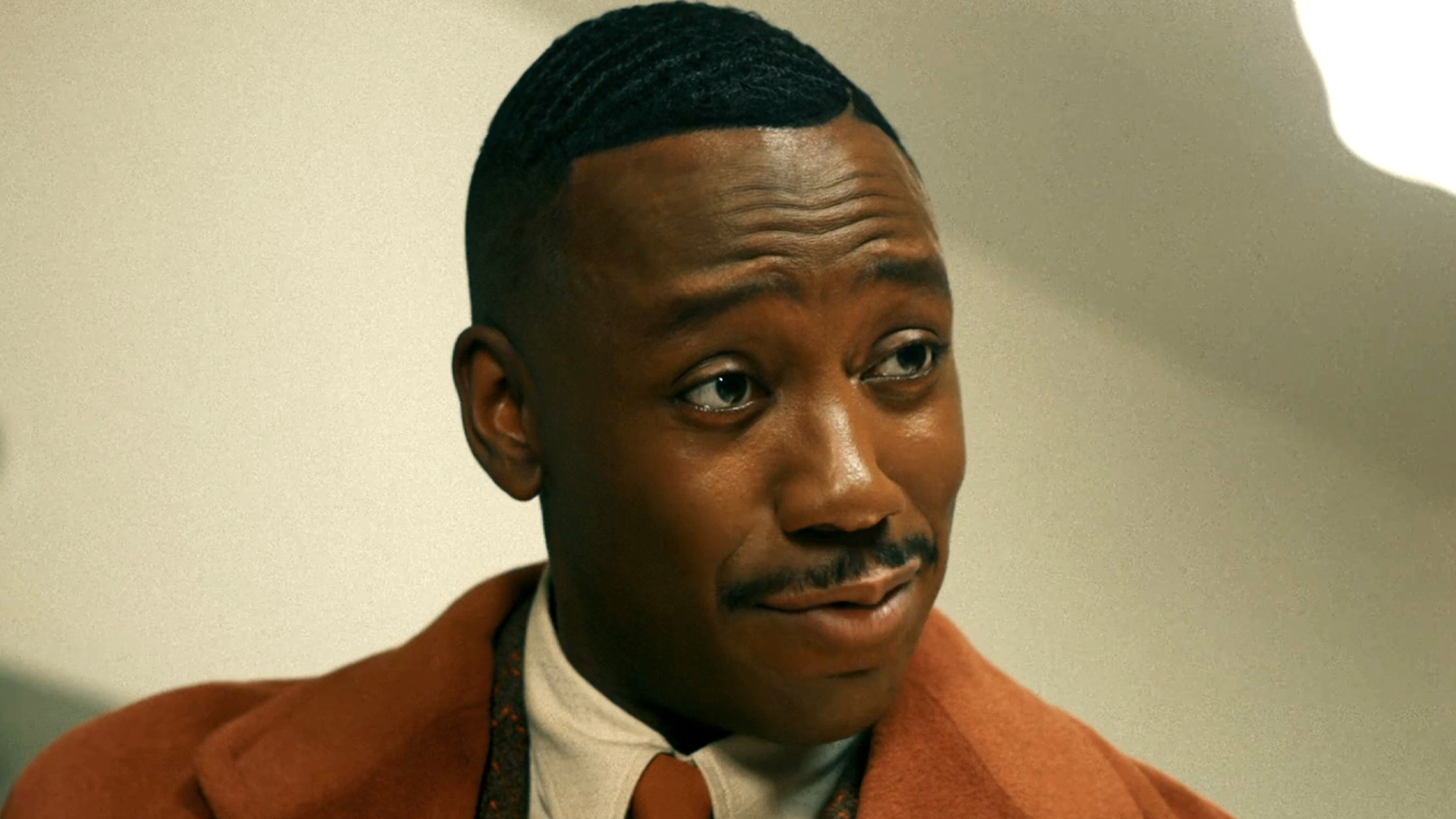 Lamorne Morris in a burnt orange suit and tie, as Robbie in Spider-Noir (2026).