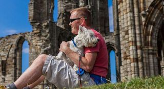 A man sitting with his dog in front of Whitby Abbey