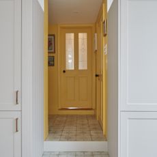A sunny yellow hallway with a matching front door seen from a white kitchen