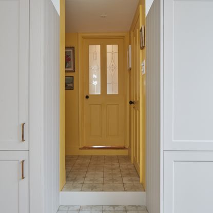 A sunny yellow hallway with a matching front door seen from a white kitchen