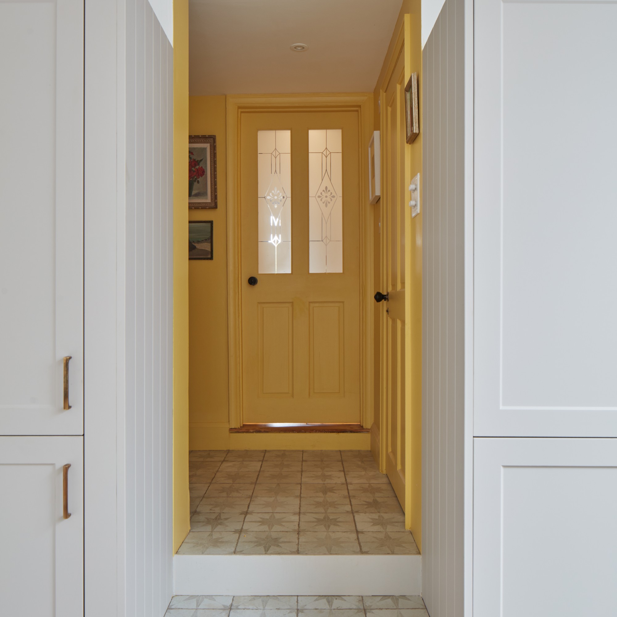A sunny yellow hallway with a matching front door seen from a white kitchen