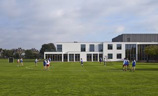 School building behind a sports field with girls playing hockey